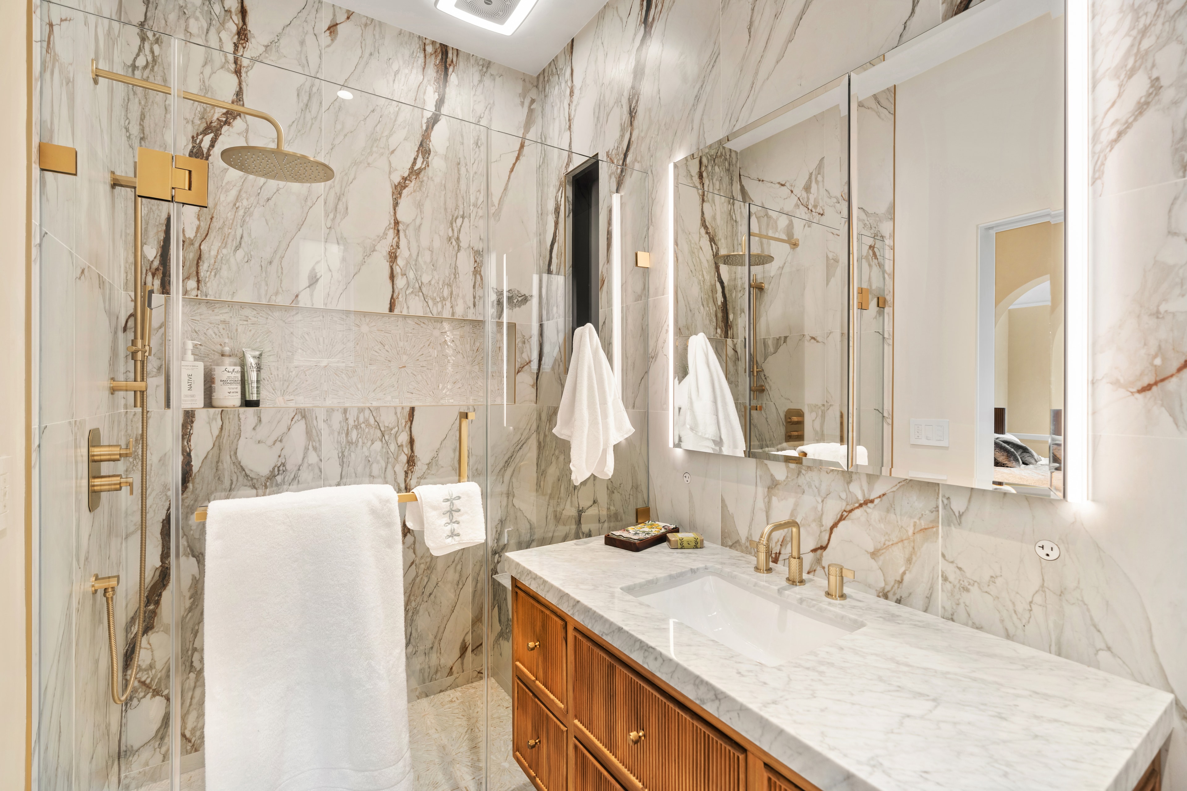 Full marble bathroom with gold fixtures and wood vanity